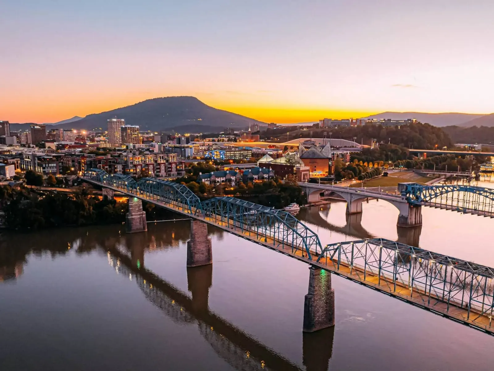 The Walnut Street Bridge crossing the Tennessee River into downtown Chattanooga at sunset, with Lookout Mountain on the horizon