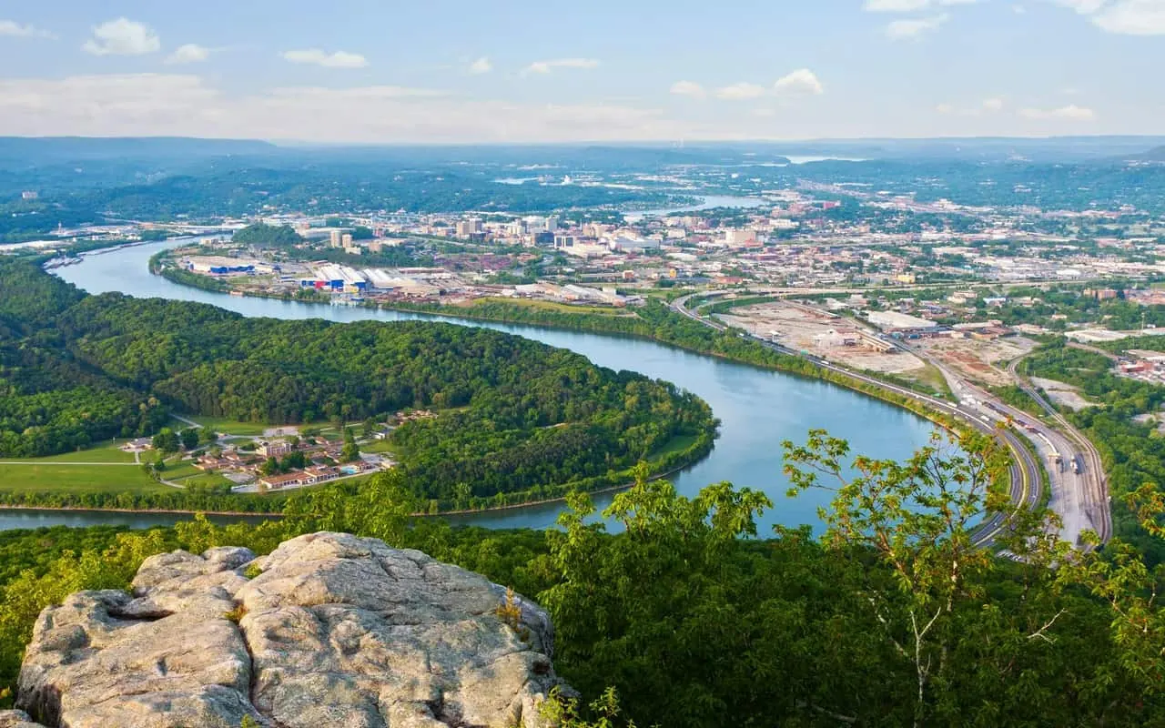 View from a rocky ridge overlook of the Tennessee River curving through wooded bottomland toward the Chattanooga riverfront