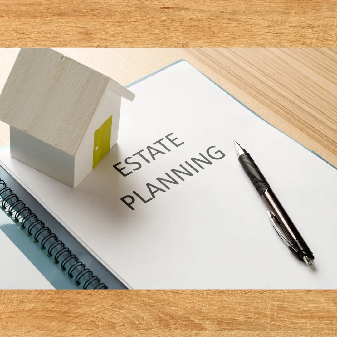 A small model house resting on a binder labeled Estate Planning, with a pen on a wooden desk