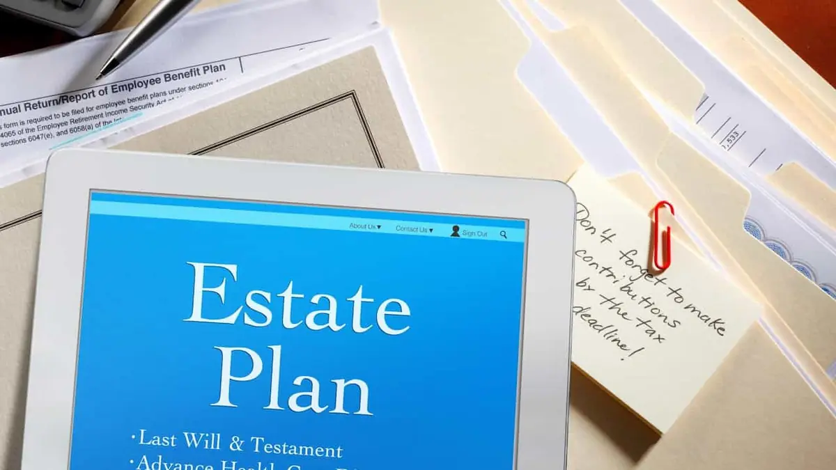 A tablet showing an estate plan checklist on a stack of folders and financial forms, with a handwritten reminder note