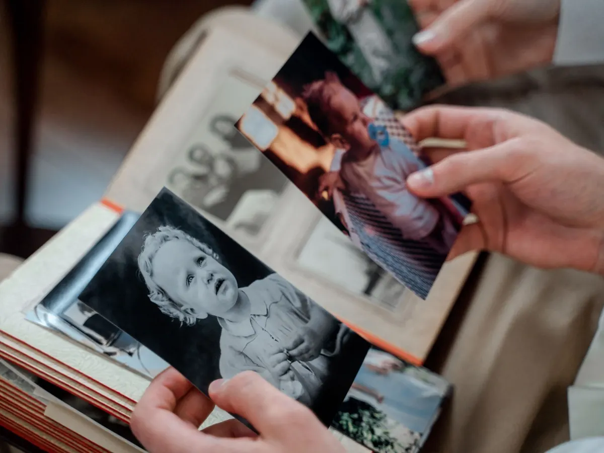 Hands hold an old black and white baby photograph over an open family album filled with snapshots.