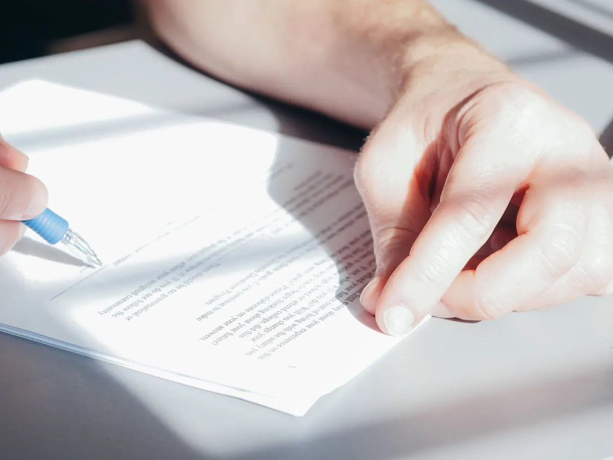 Close view of hands holding a pen over a printed agreement on a desk in soft daylight.