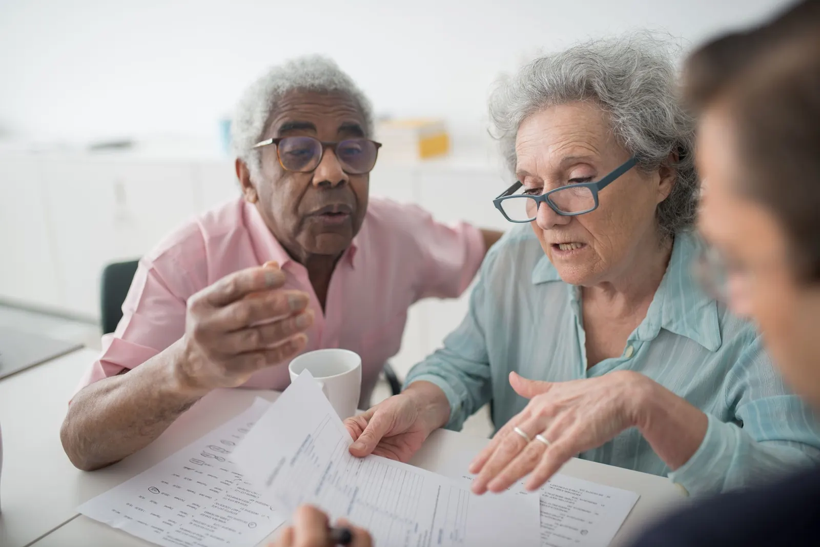 An older couple talks through paperwork at a table with an advisor seen from behind, the wife pointing to a page.