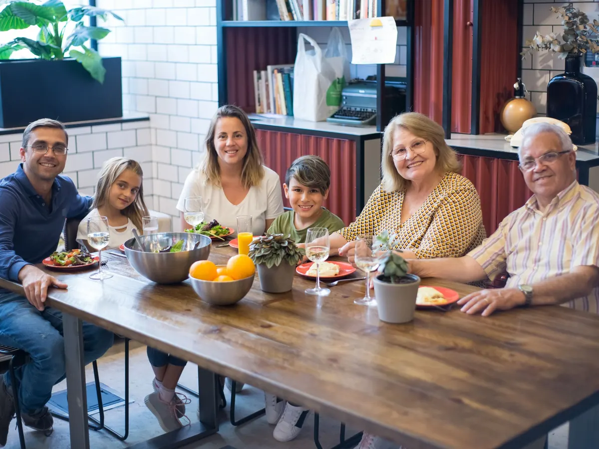 Three generations of a family share a meal around a long wooden dining table at home.